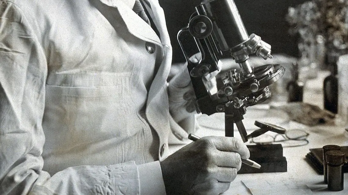 Scientist in white lab coat taking notes next to a microscope